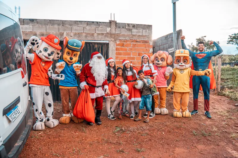 Papai Noel e personagens fantasiados com voluntários em frente a uma casa